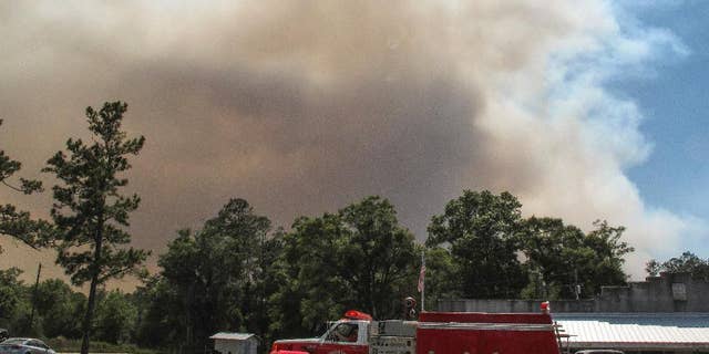 A fire truck passes as a plume of smoke rising from a wildfire burning, Monday, May 8, 2017, just outside the town of St. George, Ga. Officials placed the town under a mandatory evacuation after winds pushed the fire out of the neighboring Okefenokee National Wildlife Refuge, where a lightning strike started the blaze a month earlier. (AP Photo/Russ Bynum)