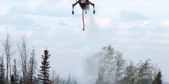 A helicopter drops water on hot spots along the highway to Fort McMurray, Canada, Sunday, May 8, 2016. (Ryan Remiorz/The Canadian Press via AP) MANDATORY CREDIT