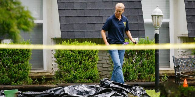 FILE - In this July 23, 2015 file photo, an investigator walks past a tarp covering a body in the front yard of a house in Broken Arrow, Okla. The Oklahoma medical examiner's office says, Monday, July 27, 2015, all five members of a Broken Arrow family killed last week died from multiple sharp-force injuries, and police have said two knives and a small hatchet were found at the scene. (AP Photo/Sue Ogrocki, File)