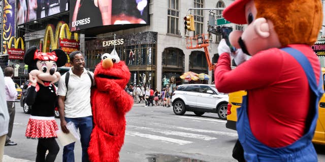 A visitor to Times Square poses for photos with iconic costumed characters, Monday, July 28, 2014, in New York. New York Mayor Bill de Blasio said Monday that he believes the people wearing character costumes in Times Square should be licensed and regulated. (AP Photo/Rachelle Blidner)
