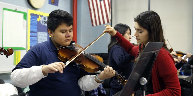 FILE - In this Dec. 12, 2014 file photo, music teacher Maria Pulido, right, works with Brian Gonzalez on his violin at the Richard Edwards Elementary School in Chicago, Illinois. Chicago now joins dozens of school districts across the country that teach mariachi music in schools. It's a way to connect schools and parents, many who speak Spanish, from Hispanic communities, say organizers. (AP Photo/Charles Rex Arbogast, File)