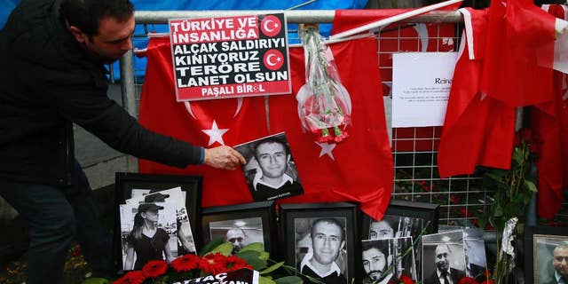 A man adjusts a victim's photograph displayed with floral tributes and Turkish flags, outside the Reina night club following the New Year's day attack, in Istanbul, Wednesday, Jan. 4, 2017. Turkey has identified the gunman in the Istanbul nightclub massacre, the foreign minister said Wednesday as the president vowed that the country won't surrender to terrorists or become divided. (AP Photo/Emrah Gurel)