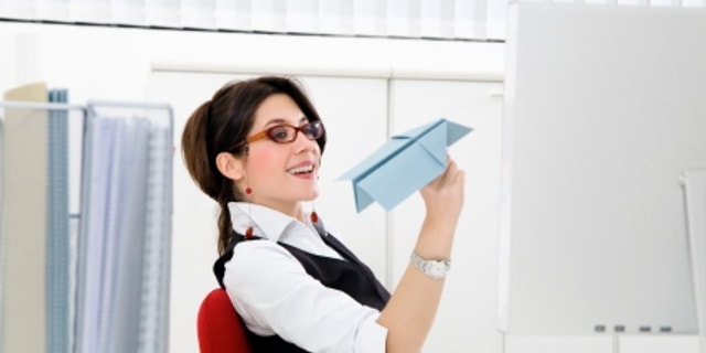 Young businesswoman throwing paper airplane in office
