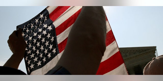 WASHINGTON, DC - JUNE 28: A protester holds an American flag during a demonstration in front of the U.S. Supreme Court, on June 28, 2012 in Washington, DC. Today the high court is expected to rule on the constitutionality of the sweeping health care law championed by President Barack Obama. (Photo by Mark Wilson/Getty Images)