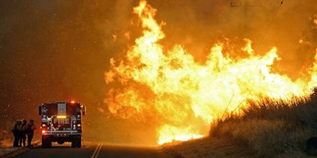 Firefighters from the Lompoc City Fire Department take shelter behind their engine Thursday, June 16, 2016, as wind driven flames advance from the Sherpa Fire.  The flames were crossing Calle Real near El Capitan State Park in Santa Barbara County. (Mike Eliason/Santa Barbara County Fire Department via AP)