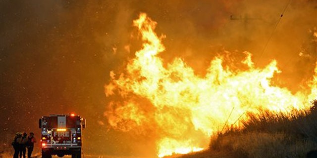 Firefighters from the Lompoc City Fire Department take shelter behind their engine Thursday, June 16, 2016, as wind driven flames advance from the Sherpa Fire. The flames were crossing Calle Real near El Capitan State Park in Santa Barbara County. (Mike Eliason/Santa Barbara County Fire Department via AP)