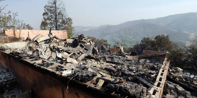 A firefighting helicopter carries a large water bucket behind a home that has been destroyed by a fire in Lake Hughes, Calif., in this June 2, 2013, photo.