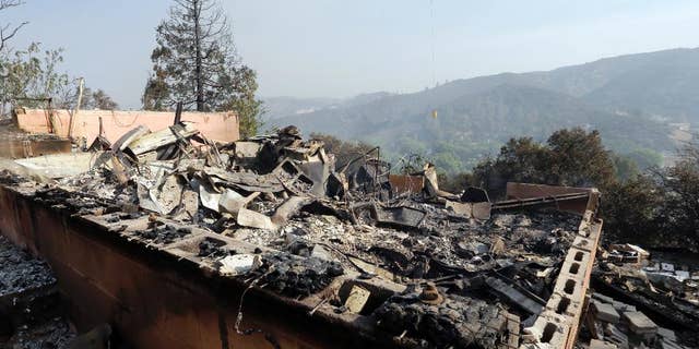 A firefighting helicopter carries a large water bucket behind a home that has been destroyed by a fire in Lake Hughes, Calif., in this June 2, 2013, photo.