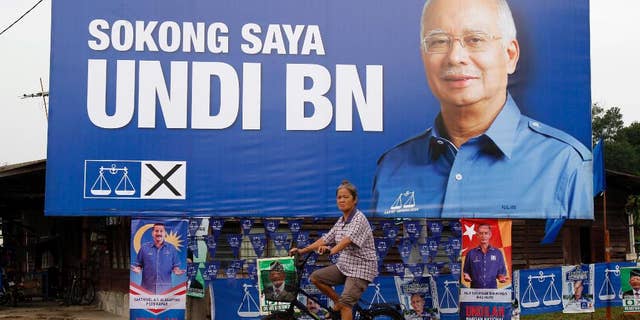 FILE - In this May 3, 2013 file photo, a Malaysian ethnic Chinese woman rides past a billboard of Malaysia's ruling National Front coalition with a portrait of Prime Minister Najib Razak which translates "I vote for National Front coalition" ahead of the upcoming general elections in Klang, outside Kuala Lumpur, Malaysia. The party of Malaysia's scandal-tainted Prime Minister Najib Razak has won two parliamentary by-elections in a landslide, further strengthening his rule despite corruption allegations. (AP Photo/Lai Seng Sin, File)