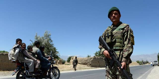 Men on a motorcycle drive past Afghan soldiers on guard outside Bagram military base, 50 kms north of Kabul, on June 19, 2013