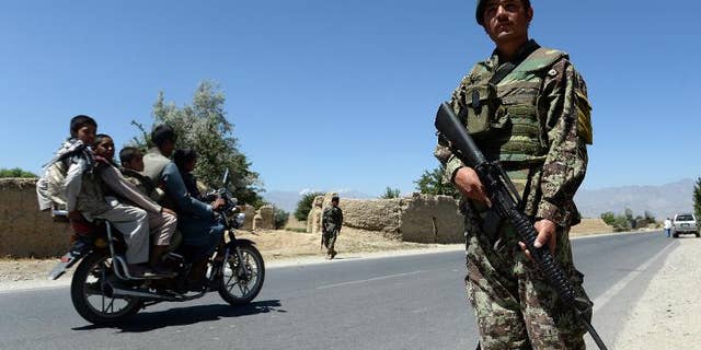 Men on a motorcycle drive past Afghan soldiers on guard outside Bagram military base, 50 kms north of Kabul, on June 19, 2013