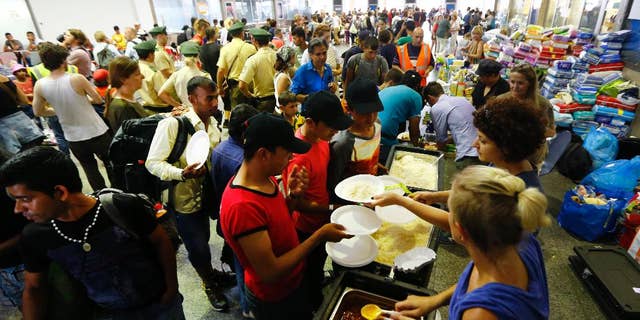 FILE - In this Sept. 1, 2015 file picture volunteers distribute  food  for migrants coming from Budapest at the main station in Munich, Germany. German weekly Der Spiegel reports Saturday May 14, 2016 the federal government expects to spend 93.6 billion euros ( US $106.22 billion) to support refugees over the next five years.  Der Spiegel cited a finance ministry document according to which much of the money will go toward basic benefit, housing support and language lessons for hundreds of thousands of asylum seekers who have come to Germany.  (AP Photo/Matthias Schrader,file)