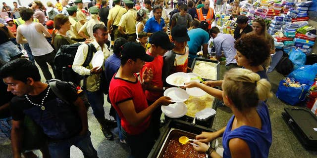FILE - In this Sept. 1, 2015 file picture volunteers distribute food for migrants coming from Budapest at the main station in Munich, Germany. German weekly Der Spiegel reports Saturday May 14, 2016 the federal government expects to spend 93.6 billion euros ( US $106.22 billion) to support refugees over the next five years. Der Spiegel cited a finance ministry document according to which much of the money will go toward basic benefit, housing support and language lessons for hundreds of thousands of asylum seekers who have come to Germany. (AP Photo/Matthias Schrader,file)