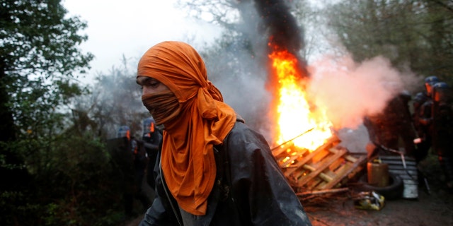 A protester walks past burning debris as French gendarmes continue an evacuation operation.