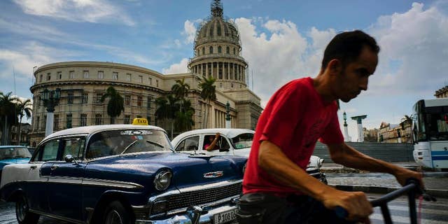 A man cycles alongside taxi drivers near the Capitol building in Havana, Cuba, Friday, July 15, 2016. Authorities warned they will pull the licenses of private taxi drivers who raise fares, after people complained that rates have doubled on some routes. Collective taxis cost about 40 cents. The warning comes as officials say the country faces months of economic and energy restrictions due in part to the crisis in Venezuela and a reduction in the amount of oil Cuba receives from its South American ally. (AP Photo/Ramon Espinosa)