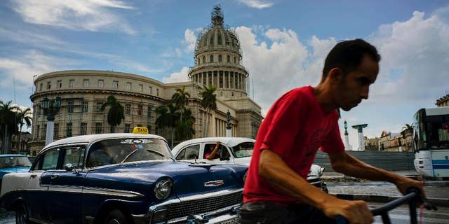 A man cycles alongside taxi drivers near the Capitol building in Havana, Cuba, Friday, July 15, 2016. Authorities warned they will pull the licenses of private taxi drivers who raise fares, after people complained that rates have doubled on some routes. Collective taxis cost about 40 cents. The warning comes as officials say the country faces months of economic and energy restrictions due in part to the crisis in Venezuela and a reduction in the amount of oil Cuba receives from its South American ally. (AP Photo/Ramon Espinosa)