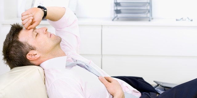 Mid-adult businessman lying on sofa at office, looking tired, eyes closed. Bright background.