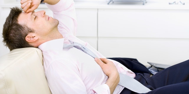 Mid-adult businessman lying on sofa at office, looking tired, eyes closed. Bright background.