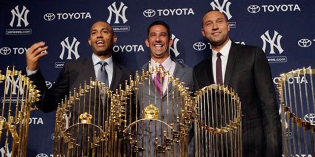 New York Yankees baseball player Jorge Posada, center, is flanked by teammates Mariano Rivera, left, and Derek Jeter, as he stands behind five World Series trophies at a press conference to announce his retirement at Yankee Stadium in New York on Tuesday, January 24.  , 2012.