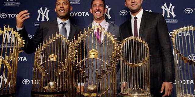 New York Yankees baseball player Jorge Posada, center, is flanked by teammates Mariano Rivera, left, and Derek Jeter, as he stands behind five World Series trophies at a press conference to announce his retirement at Yankee Stadium in New York on Tuesday, January 24.  , 2012.