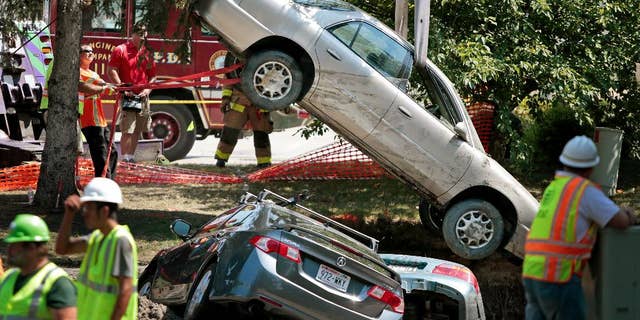 Towing company workers lift one of three cars out of a sinkhole in the parking lot of an apartment complex, Friday, Aug. 14, 2015, in Madison, Wis. About 300 residents of the complex were evacuated after a water pipe break created the sinkhole and potential gas leak. (Michael P. King/Wisconsin State Journal via AP) MANDATORY CREDIT