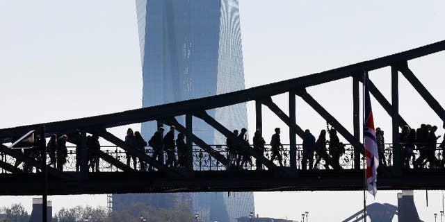 People walk over a bridge near the European Central Bank (background) in Frankfurt, Germany, Monday, May 2, 2016. (AP Photo/Michael Probst)