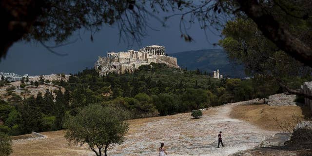 Tourist walk on Pnyx hill in front the ancient Acropolis hill, with the ruins of the fifth century BC Parthenon temple in Athens on Tuesday, June 7, 2016. Beginning as early as 507 BC, the Athenians gathered on the Pnyx to host their popular assemblies, thus making the hill one of the earliest and most important sites in the creation of democracy.(AP Photo/Petros Giannakouris)