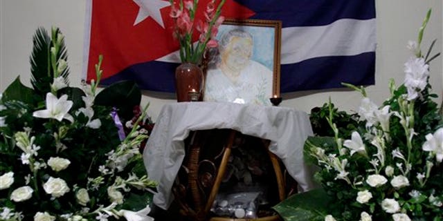 A painting of Laura Pollan, late leader of the dissident group Ladies in White, is flanked by flowers, candles and a Cuban flag during a gathering in her honor at her home in Havana, Cuba, Saturday Oct. 15, 2011.