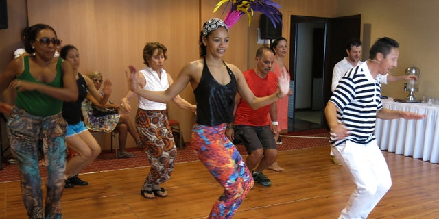 Nete Vieira, center, and her husband Naldi, right, teach samba to foreigners in Rio de Janeiro, Sunday, Feb. 15, 2015. There is a self-deprecating phrase Brazilians with poor dancing skills use to explain their awkwardness at the parades during Carnival: I samba like a foreigner. But even foreigners visiting Brazil for Carnival celebrations can learn a few basic moves thanks to the patience of dancing duo Nete Vieira and her husband Naldi. They teach the basics of rhythmic bouncing, marching and arm waving that will help newcomers have fun, and feel less intimidated, while joining the raucous parties that crowd the streets of Rio de Janeiro. (AP Photo/Adriana Gomez)
