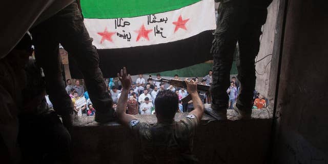 In this Friday, Sept. 21, 2012 file photo, Free Syrian Army rebels hold a revolutionary flag during a demonstration in the Bustan al-Qasr neighborhood of Aleppo, Syria.