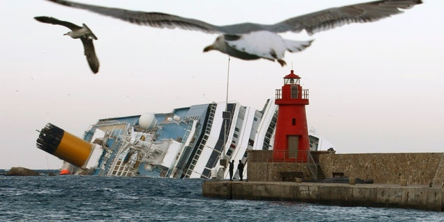 FILE - In this , Monday, Jan. 30, 2012 file photo, seagulls fly in front of the grounded cruise ship Costa Concordia off the Tuscan island of Giglio, Italy. As if the nightmares, flashbacks and anxiety weren't enough, passengers who survived the terrifying grounding and capsizing of the Costa Concordia off Tuscany have come in for a rude shock as they mark the first anniversary of the disaster on Sunday, Jan. 13, 2013. Ship owner Costa Crociere SpA, the Italian unit of Miami-based Carnival Corp., sent several passengers a letter telling them they weren't welcome at the official anniversary ceremonies on the island of Giglio where the hulking ship still rests. Costa says the day is focused on the families of the 32 people who died Jan. 13, 2012, not the 4,200 passengers and crew who survived. (AP Photo/Pier Paolo Cito, File)