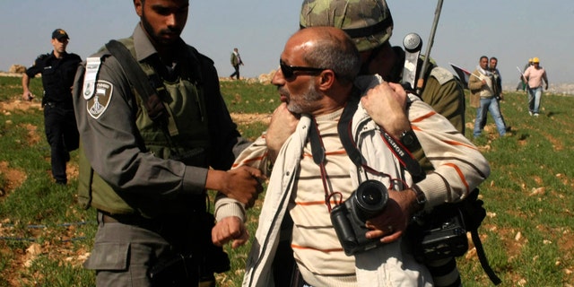 In this Saturday Feb. 9, 2013 photo, Israeli security detain The Associated Press photographer Nasser Shiyoukhi during a Palestinian protest in Yatta, West Bank. Israeli troops detained Shiyoukhi handcuffing him and forcing him to sit on the ground without food or water or access to a bathroom for roughly five hours, according to witness accounts. Shiyoukhi was released without charge after Saturday’s incident. (AP Photo)
