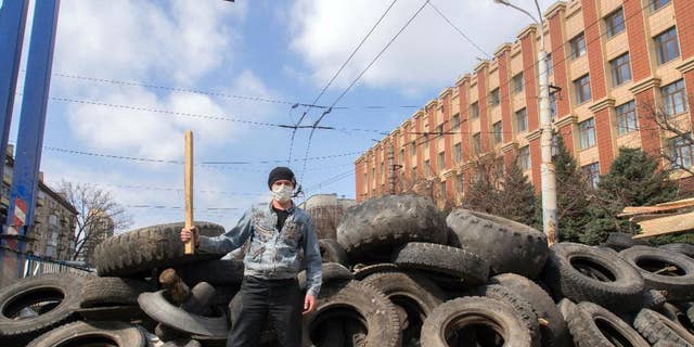 A masked pro-Russian activist poses for a photo in front of barricades at the Ukrainian regional office of the Security Service in Luhansk, 30 kilometers (20 miles) west of the Russian border, in Ukraine, Wednesday, April 9, 2014. Ukrainian Interior Minister Arsen Avakov said the standoff in Luhansk and the two neighboring Russian-leaning regions of Donetsk and Kharkiv must be resolved within two days.(AP Photo/Igor Golovniov)