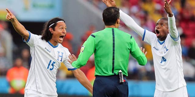 10ThingstoSeeSports - Honduras players Roger Espinoza, left, and Luis Garrido complain to referee Sandro Ricci from Brazil after he awarded a goal to France using goal line technology during the group E World Cup soccer match between France and Honduras at the Estadio Beira-Rio in Porto Alegre, Brazil, Sunday, June 15, 2014. (AP Photo/David Vincent, File)