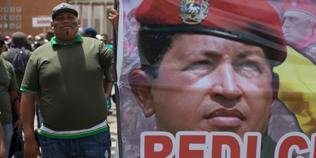 A supporters of Venezuela's President Nicolas Maduro stands next to a picture of Venezuela's late President Hugo Chavez prior a civilian and military exercise at fort Tiuna in Caracas, Venezuela, Saturday, March 14, 2015. President Maduro is expected to oversee military exercises across the country, which are intended to show the South American countryâs strength in the face of U.S. threats. (AP Photo/Fernando Llano)