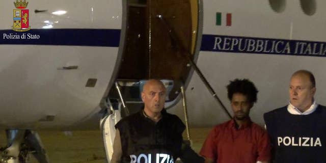 This photo taken from a video and released by the Italian Police shows Medhane Yehdego Mered, center,  a 35-year-old Eritrean, arrested two weeks ago in Sudan, upon his arrival at Ciampino's airport, in the outskirts of Rome, late Tuesday June 7, 2016.  Italy for the first time has taken custody of one of the alleged organizers of a people-smuggling route through Africa that has moved hundreds of millions of euros across borders and tens of thousands of migrants to Europe. (Italian Police via AP)