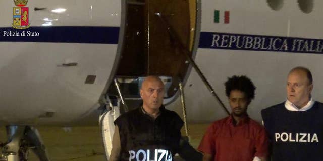This photo taken from a video and released by the Italian Police shows Medhane Yehdego Mered, center, a 35-year-old Eritrean, arrested two weeks ago in Sudan, upon his arrival at Ciampino's airport, in the outskirts of Rome, late Tuesday June 7, 2016. Italy for the first time has taken custody of one of the alleged organizers of a people-smuggling route through Africa that has moved hundreds of millions of euros across borders and tens of thousands of migrants to Europe. (Italian Police via AP)