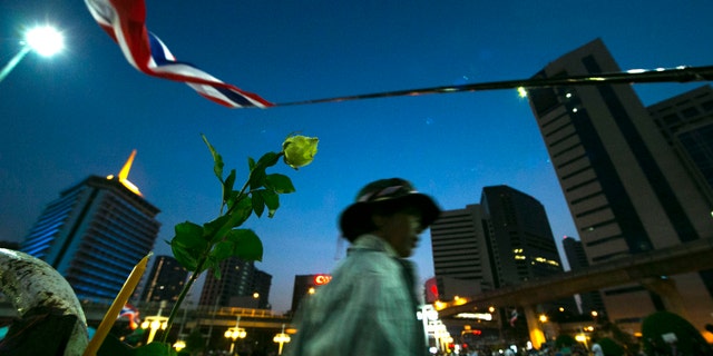 An anti-government protester walks past a flower during a condolence ceremony for the slain protester Prakong Chujan who died in Friday's grenade attack at Lumpini rally site in Bangkok, Thailand Saturday, Jan. 18, 2014. A grenade thrown into a crowd of marching anti-government demonstrators in Thailand's capital killed one man and wounded dozens of people, an ominous development that raises tensions in the country's political crisis and the specter of more bloodshed to come. (AP Photo/Wason Wanichakorn)