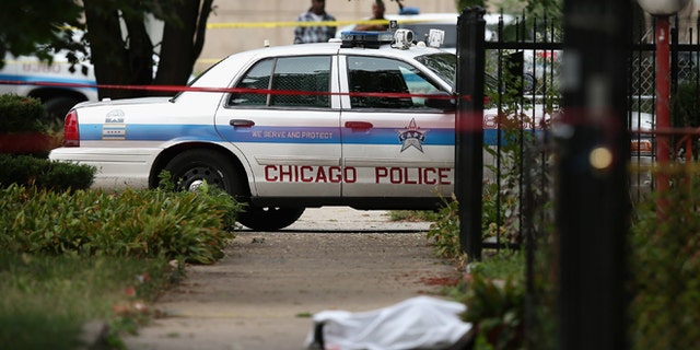 Police investigate the shooting death of 14-year-old Tommy McNeal, whose body is covered by a sheet on the sidewalk on September 20, 2013 in Chicago, Illinois. (Photo by Scott Olson/Getty Images)