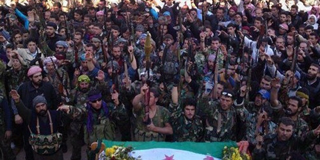 Feb. 2, 2012: In this image, provided by the Local Coordination Committees in Syria, Syrian rebels raise their weapons as they attend a funeral procession of their comrade, whose dead body, front, is seen wrapped by the Syrian revolution flag, in Edleb, north Syria.