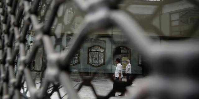 People are reflected on the glass of a shuttered shop as they walk in a shopping arcade, in central Athens, on Monday, May 25, 2015. Greece's radical left-led government has ruled out restricting access to bank accounts and the free movement of capital if there is no breakthrough soon in tortuous negotiations with bailout creditors and the country runs out of money. (AP Photo/Petros Giannakouris)