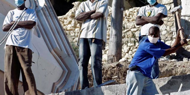 Jan. 14: Young men stand watch as another digs through debris in the shattered Haitian capital of Port-au-Prince. Tensions are rising as aid slowly filters in.