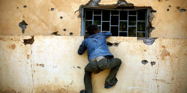 A Malian boy climbs the wall of the police station in Gao, northern Mali, Monday, Feb. 11, 2013, one day after Mujao fighters engaged in a firefight with Malian forces. French and Malian government forces have regained control of this northern city, after Islamic fighters fought a prolonged battle. Hospital officials and witnesses say three civilians died in the fighting Sunday. It is not known how many extremists and Malian troops died in the more than five hours of combat. (AP Photo/Jerome Delay)