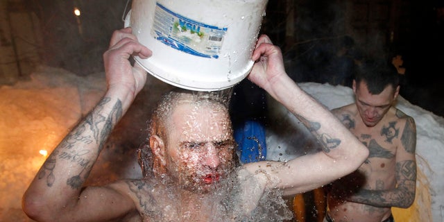 FILE - In this file photo dated Thursday, Jan. 19, 2012, inmates of a prison colony pour cold water over themselves to celebrate Epiphany at St. Peter and Paul Cathedral in the Murmansk region of northern Russia. The contract-style killing of Russian mobster Aslan Usoyan, also known as Grandpa Khasan, on Wednesday Jan16, 2013, drew renewed attention to the extensive and elaborate culture of the country’s underworld figures who call themselves “crowned thieves” and “thieves in law.” Only top criminals are allowed to have tattoos which signal their privileged status within the criminal underworld, and may contain obscure codes, such as MIR (peace) meaning “Only capital punishment will correct me, and the Nazi swastika means rejection of everything Soviet (but does not make its bearer a neo-Nazi). (AP Photo/ Andrey Pronin, FILE)