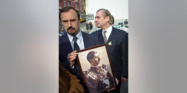 FILE - In this Feb.13 2003, file picture an unidentified man holds a photograph of Romania's King Carol II as Romania's Prince Paul, right, walks past outside a church in Lisbon, Portugal, where the king was buried. Prosecutors have detained Romania's Prince Paul, Friday, Dec. 11, 2015, in a case of alleged real estate fraud involving a top aide to a former prime minister and a newspaper editor.(AP Photo/Armando Franca, File)