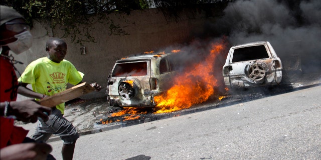 People run after cars were set on fire near the Best Western hotel during protests over a fuel price increase in Port-au-Prince, Haiti, on Saturday, July 7, 2018.