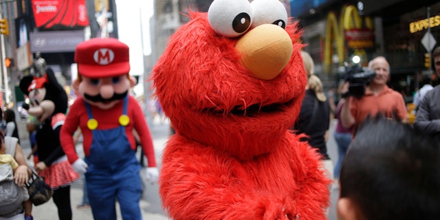 A person dressed as Elmo shakes hands with a pedestrian in Times Square on Monday, July 28, 2014 in New York. New York City Mayor Bill de Blasio said Monday that he believes the people wearing character costumes in Times Square should be licensed and regulated. Dozens of people dressed as kids favorites like Elmo, Cookie Monster and Batman stand near 42nd Street and pose for photos with tourists in exchange for money. De Blasio said the practice has gone too far. A man dressed as Spider-man was arrested Saturday, July 28, 2014, after punching a police officer who told him to stop harassing tourists. The City Council is working on legislation that would require the characters to get a city-approved license. (AP Photo/Seth Wenig)