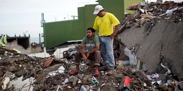 Roberto Ganchoso is comforted by a neighbor as he sits on what's left of his neighborhood, as he watches a bulldozer demolish the hotel next door to his property in Pedernales, Ecuador, Saturday, April 23, 2016. President Rafael Correa has said the earthquake caused $3 billion in damage and warned that the reconstruction effort will take years. His administration is temporarily raising taxes to fund the recovery. (AP Photo/Rodrigo Abd)