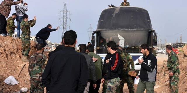 In this photo released by the Syrian official news agency SANA, Syrian government forces welcome a bus carry Syrian citizens and pro-government fighters who evacuated from the two pro-government villages of Foua and Kfarya, upon their arrival at a cross point between the rebels and the Syrian government forces on the outskirts of Aleppo city, Syria, Friday, April, 21, 2017. Syrian state TV says the troubled population transfers involving thousands of Syrians have resumed after stalling for days following a massive explosion that killed dozens. (SANA via AP)