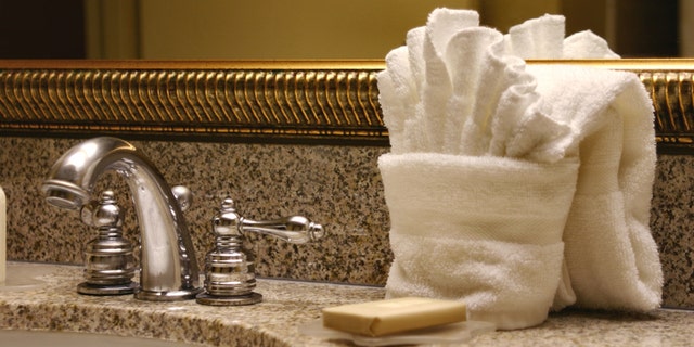 Hotel sink with soap and folded washcloth, towel, and mirror. Horizontal image.